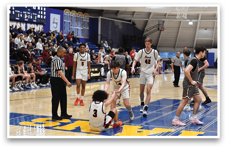 A group of people are playing basketball on a court. One person is sitting on the ground, while others are standing around him. A referee is present, observing the game. AI generated content