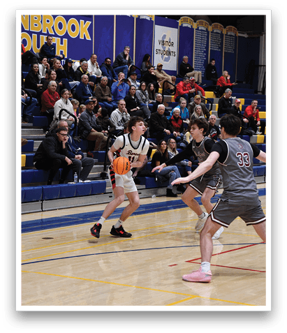 A basketball game is taking place with players on the court. A boy is holding a basketball and is about to shoot it. There are several other players on the court, some of them are wearing uniforms. The audience is watching the game from the stands. AI generated content