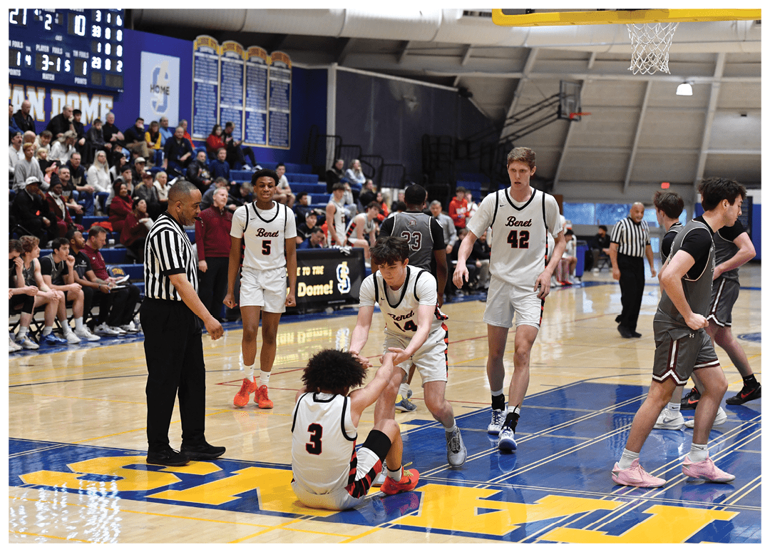 A group of people are playing basketball on a court. One person is sitting on the ground, while others are standing around him. A referee is present, observing the game. AI generated content
