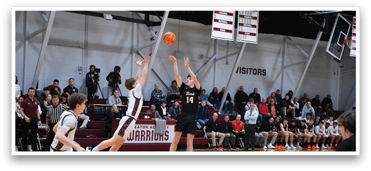 A basketball game is in progress with players on the court. A man is jumping to catch the ball while another player tries to block him. The crowd watches intently from the stands. AI generated content
