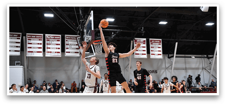 A basketball game is in progress with two teams playing. One player is jumping to block a shot, while another player is attempting to score. The game is being watched by a crowd of spectators. AI generated content
