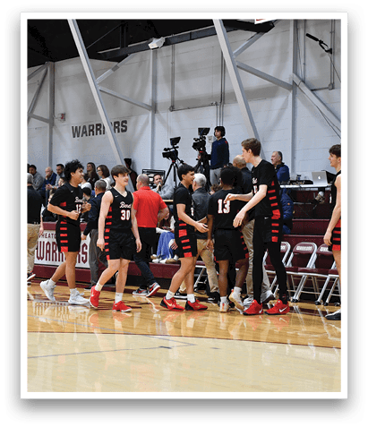 A group of young men wearing black and red uniforms are standing on a basketball court. They are holding hands and hugging each other, possibly celebrating a victory or showing support for one another. The scene takes place in a gymnasium, with a crowd of people watching the game. AI generated content