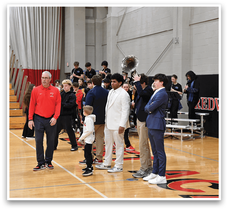 A group of people, including a man and a boy, stand on a basketball court. The man is wearing a red shirt and the boy is wearing a white shirt. The group appears to be posing for a picture. AI generated content
