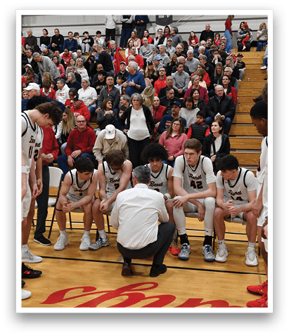 A group of young men wearing white jerseys and black shorts are standing on a basketball court. They are in the middle of a game, with some players kneeling down and others standing. The crowd is watching the game intently, with several people sitting on chairs and benches around the court. The atmosphere is lively and competitive, as the players showcase their skills and teamwork. AI generated content