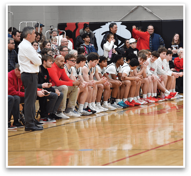 A group of people are sitting on the floor in a gym. A referee is standing over them, and a boy is holding a basketball. AI generated content