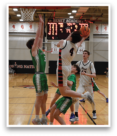 A basketball game is taking place in a gymnasium with two teams playing. One player is attempting to block a shot, while another player is reaching for the ball. The gym is filled with spectators, and the atmosphere is intense. AI generated content