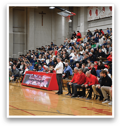 A basketball game is being played in a gym with a crowd of people watching. The players are wearing uniforms and the spectators are seated on chairs. AI generated content