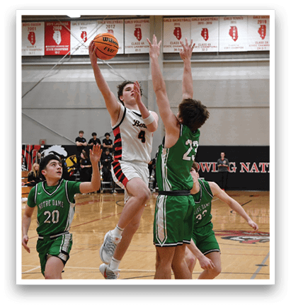 A basketball game is taking place with two teams playing against each other. One player is jumping up to block a shot, while another player is attempting to score. The game is being watched by a crowd of people. AI generated content