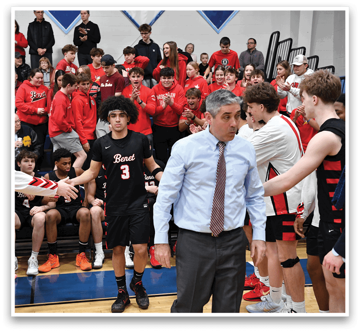 A group of people are gathered in a gym, with some of them wearing red shirts. A man in a suit is shaking hands with a man in a black shirt. The crowd is watching the interaction between the two men. AI generated content