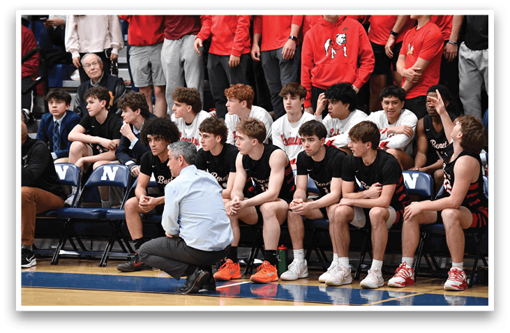 A group of boys are sitting on a bench, with one man kneeling in front of them. They are all wearing black shirts. AI generated content