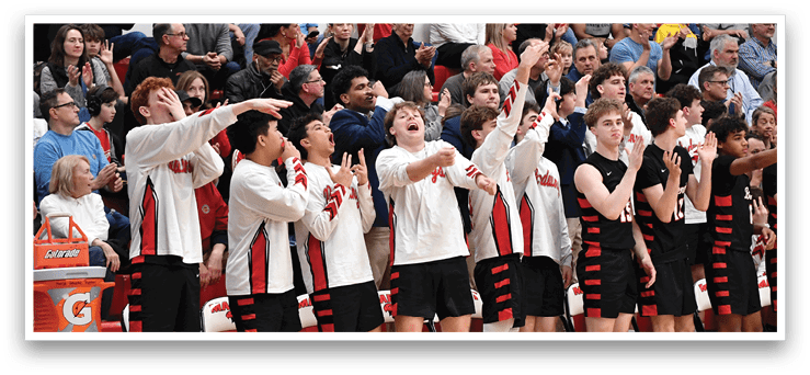 A group of young men are standing on a basketball court, holding up their hands in the air. They are wearing red and black uniforms and are surrounded by a crowd of people who are watching the game. AI generated content