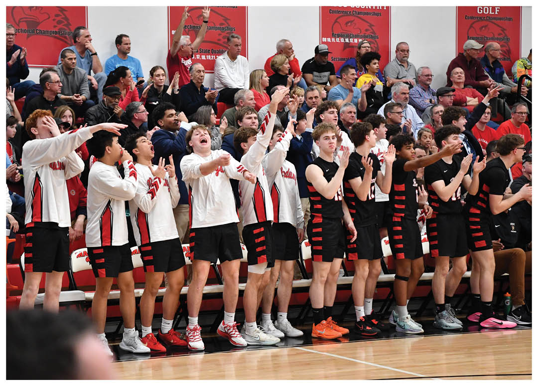 A group of young men are standing on a basketball court, holding up their hands in the air. They are wearing red and black uniforms and are surrounded by a crowd of people who are watching the game. AI generated content