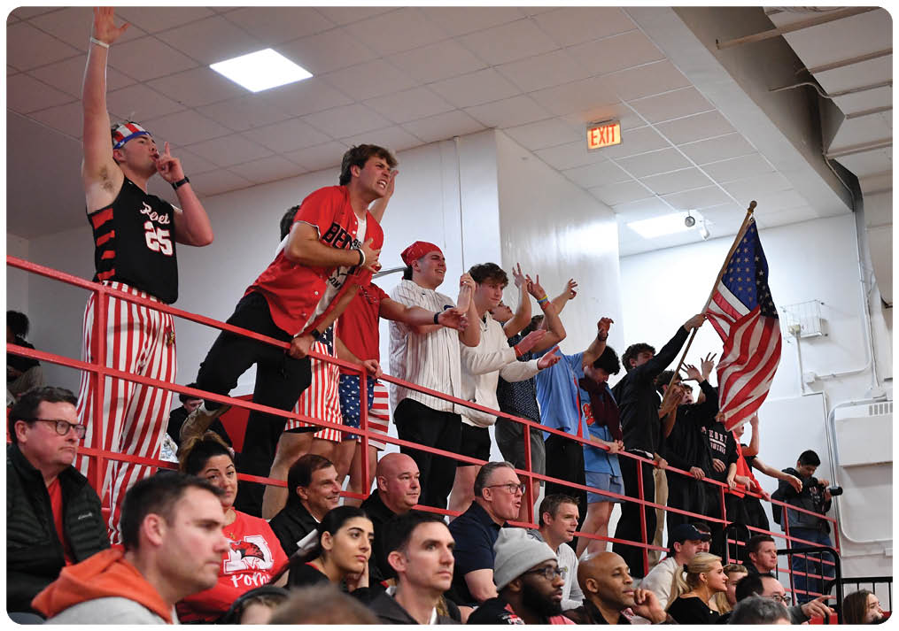 A group of people are sitting in the stands, watching a game. They are wearing red, white, and blue clothing, and some are holding American flags. The crowd is engaged and excited, cheering for their team. AI generated content