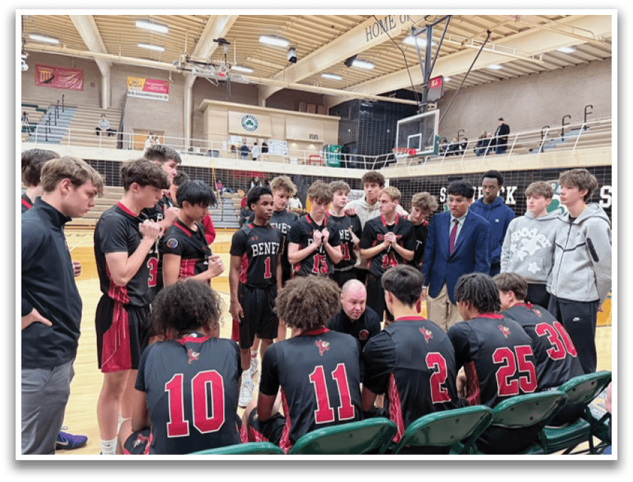 A group of young men are standing on a basketball court, wearing black shirts and shorts. They are gathered around each other, engaged in conversation. Some of the men are holding cell phones, possibly taking pictures or sharing information. The scene appears to be a casual gathering of friends or teammates, possibly discussing their next move on the court. AI generated content