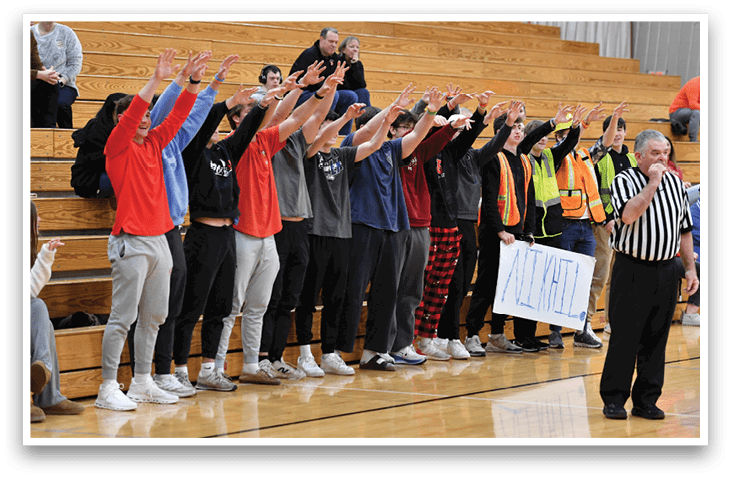 A group of people are sitting on a bench in a gym. A man in a striped shirt stands in front of them, holding up his hand. AI generated content