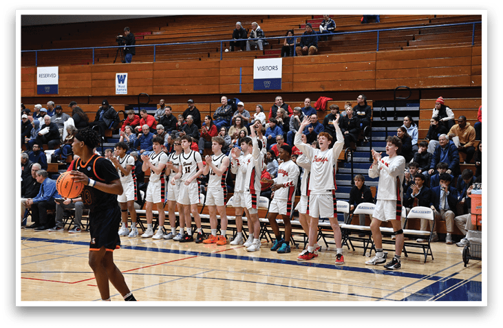 A group of young men are standing on a basketball court, some holding their hands up in the air. They are wearing uniforms and are likely celebrating a victory. The crowd is watching the game from the stands, and there are several chairs placed around the court. AI generated content