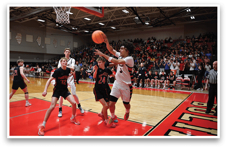 A basketball game is taking place with a player in the air trying to get the ball. The crowd is watching the game intently. AI generated content