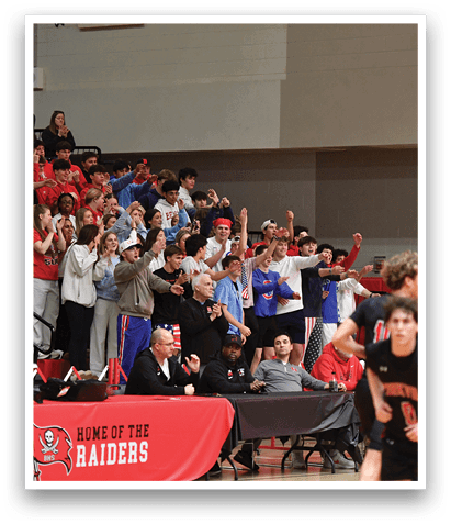 A group of people are gathered in a gym, with some of them holding up their arms. A man in a red shirt is sitting at a table, and a boy in a black shirt is running on the court. AI generated content