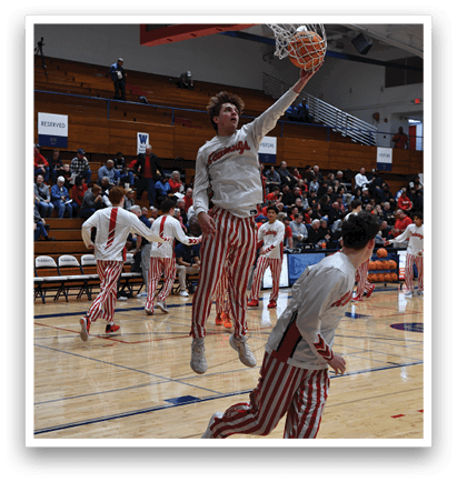 Basketball players are playing in a gym, with one player jumping to hit the ball. The crowd is watching the game, and there are several chairs placed around the gym. AI generated content
