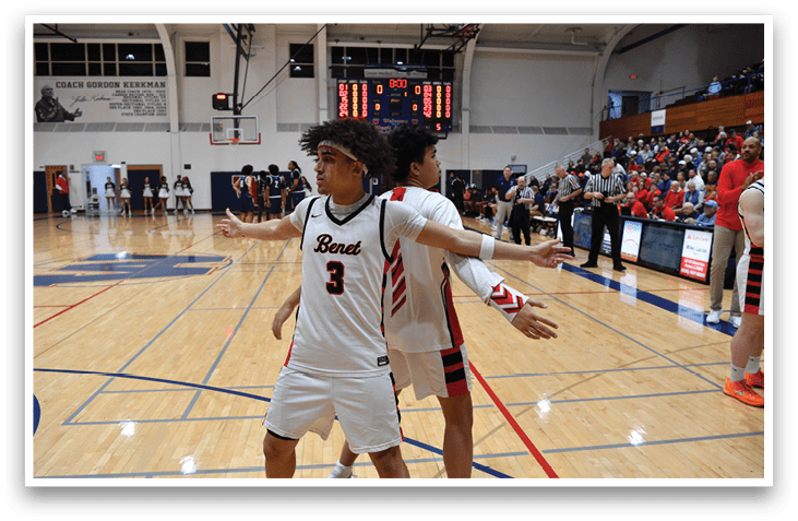 Two basketball players are on the court, one wearing a white jersey and the other wearing a red jersey. They are both holding their arms out, possibly for a high five or a hug. The players are surrounded by a crowd of people, likely spectators or teammates. AI generated content