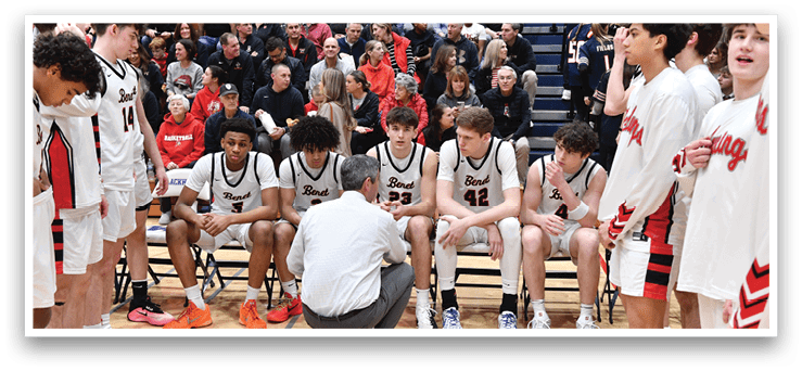A group of young men are sitting on a bench, with one man kneeling down in front of them. The group is wearing uniforms, and there is a crowd of people watching them. AI generated content