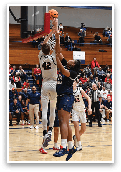 Basketball players are playing in a game. One player is jumping to block a shot. The crowd is watching the game. AI generated content