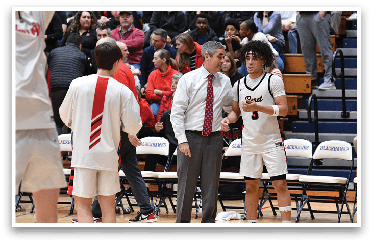 A group of men are playing basketball on a court. A man in a suit is talking to a player in a white uniform. The crowd is watching the game. AI generated content