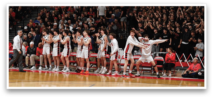 A group of young men are standing on a basketball court, some of them wearing white uniforms. They are holding their hands up in the air, possibly celebrating a victory or preparing for a game. The crowd is watching them, and there are several chairs placed around the court. AI generated content