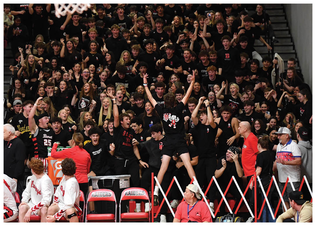A group of people are sitting on chairs in a gym, watching a basketball game. The crowd is cheering and clapping, with some standing and others sitting. The atmosphere is lively and energetic. AI generated content