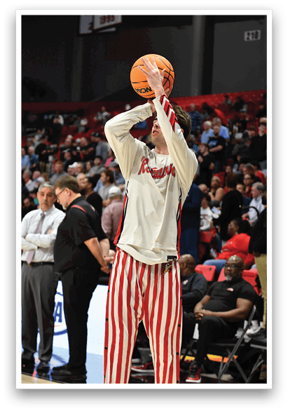 A man in a white shirt and red and white striped pants is holding a basketball in a crowded stadium. AI generated content