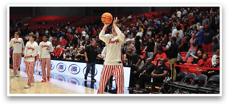 A man in a white shirt and red and white striped pants is holding a basketball in a crowded gym. AI generated content
