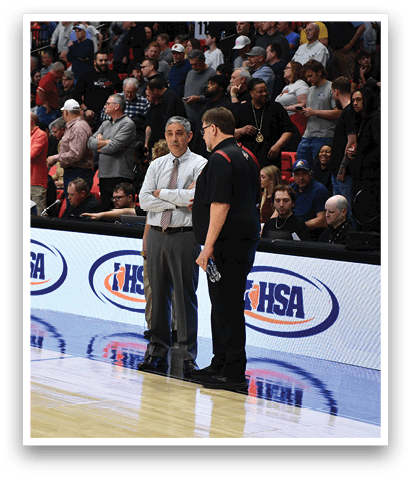 A group of men are standing on a basketball court, with one man wearing a black shirt and white pants. The other men are wearing various outfits, and some are wearing ties. The men are engaged in a conversation, and the crowd is watching the game. AI generated content