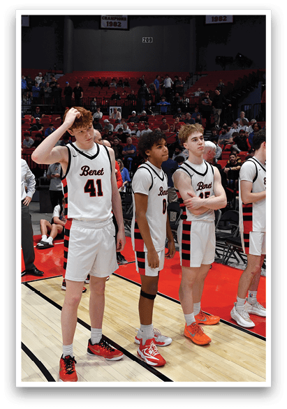 A group of basketball players are standing on a court, some of them wearing red and white uniforms. They are lined up, possibly waiting for a game to start or for their turn to play. The crowd is watching the players, and there are several chairs placed around the court. AI generated content
