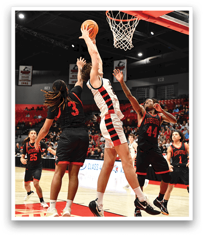A basketball game is in progress with a player jumping to block a shot. AI generated content