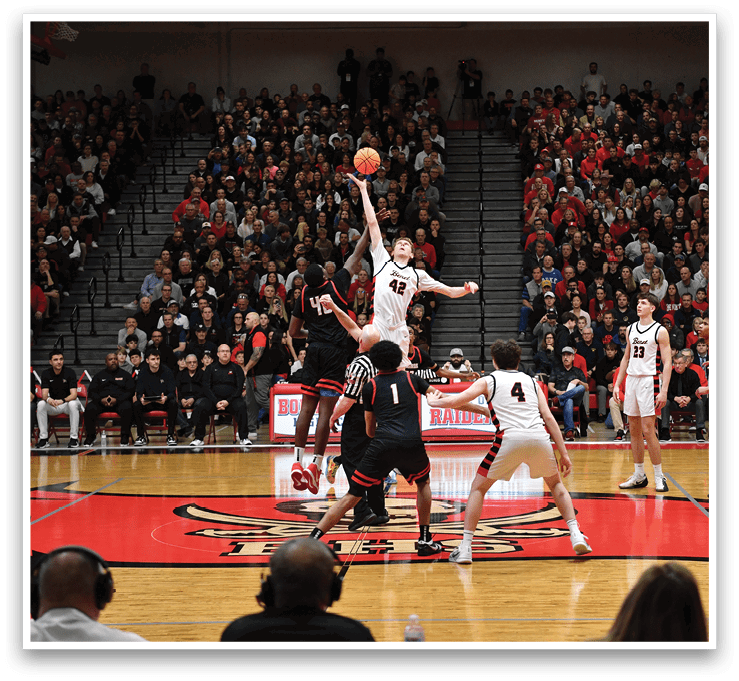 A basketball game is taking place with a player jumping to shoot the ball. The crowd is watching intently as the players compete. AI generated content