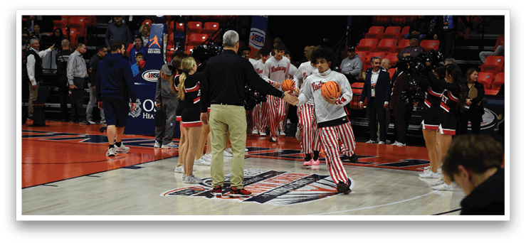 A group of people, including a man and a boy, are standing on a basketball court. The man is holding a basketball, and the boy is holding a basketball as well. The group appears to be engaged in a conversation or a game. AI generated content