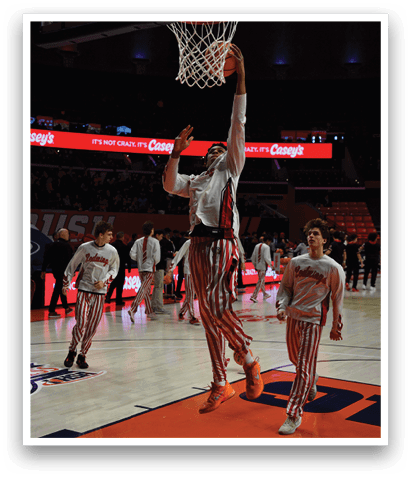 A group of men in striped pants are playing basketball. One man is dunking the ball through a basketball hoop while others are watching. AI generated content
