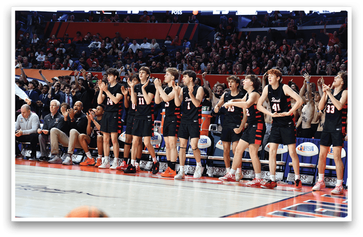 A group of young men are standing on a basketball court, wearing black and red uniforms. They are clapping and cheering, likely celebrating a victory or supporting their teammates. The crowd is watching the game, and there are several chairs placed around the court. The atmosphere is lively and energetic, with everyone engaged in the event. AI generated content