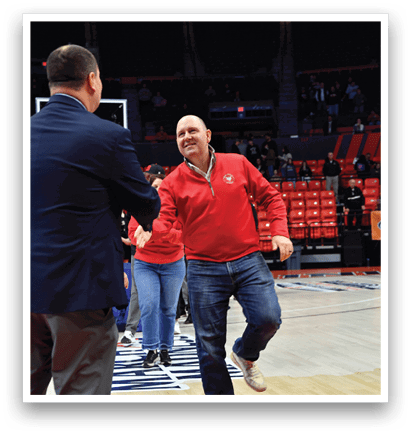 Two men are standing on a basketball court, one wearing a red shirt and the other in a suit. They are talking to each other. AI generated content