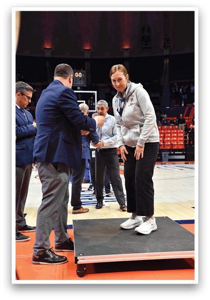 Men are standing on a basketball court, some wearing suits. A man in a suit is shaking hands with another man in a suit. AI generated content