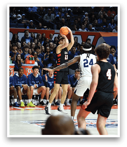 A basketball game is taking place with a player in the air attempting to score a basket. The crowd is watching intently as the player jumps to make the shot. AI generated content