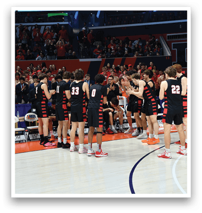 A group of men wearing black and red uniforms are standing on a basketball court. They are holding hands and hugging each other, likely celebrating a victory. The crowd is watching the players from the stands, and there are several chairs placed around the court. AI generated content