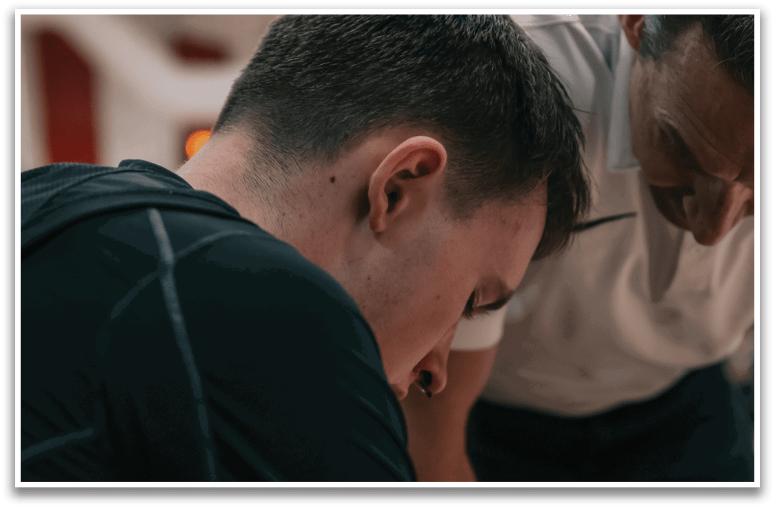 A man is sitting down with his head in his hands, while a man in a white shirt stands behind him. AI generated content