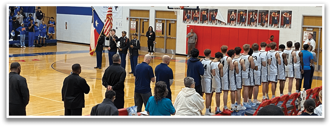 A group of people are standing on a basketball court, some of them wearing white uniforms. A man in a suit is speaking to the group, while a woman stands nearby. A flag is hanging from the ceiling, and a clock is visible on the wall. AI generated content
