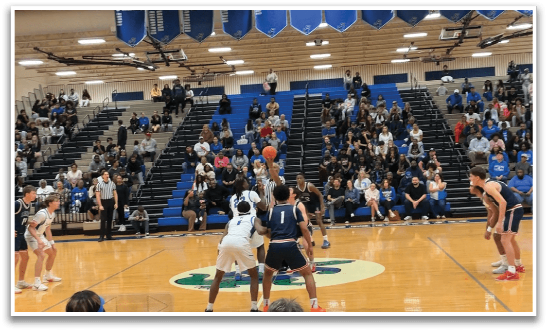 A basketball game is taking place with a group of men playing. The game is being watched by a crowd of people who are seated on chairs. The players are actively engaged in the game, with one player holding a basketball in the air. AI generated content