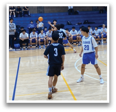 A basketball game is taking place in a gymnasium with a group of people playing. A man is holding a basketball and is about to throw it. There are several other people on the court, some of them holding basketballs as well. The gym is filled with people, and there are chairs placed around the court for spectators. AI generated content