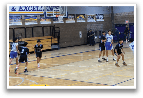 A basketball game is taking place in a gymnasium with a group of men playing. The players are wearing blue and white uniforms, and there are spectators watching the game. The gym has a basketball hoop and a bench for the players to sit on. The atmosphere is lively, and the players are actively engaged in the game. AI generated content