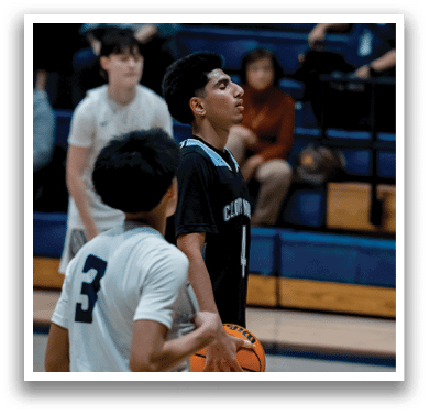 Two basketball players are on the court, one holding a basketball. A man in a black shirt is looking at the ball, possibly preparing to shoot it. There are other people in the background, possibly watching the game or waiting for their turn to play. AI generated content