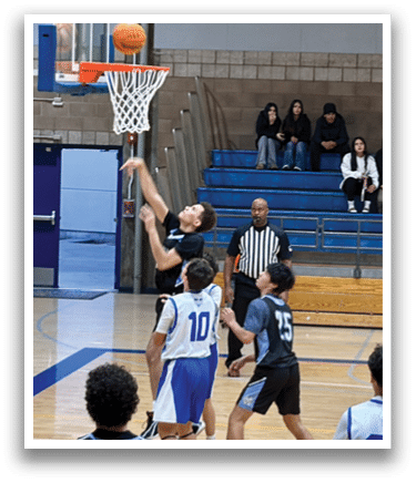 A basketball game is taking place with a player in the air attempting to score a basket. The game is being watched by a crowd of people sitting on benches. AI generated content