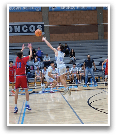 A basketball game is taking place in a gymnasium with a group of people playing. A man is in the air, attempting to dunk the basketball. The game is being played on a basketball court with a hoop. AI generated content